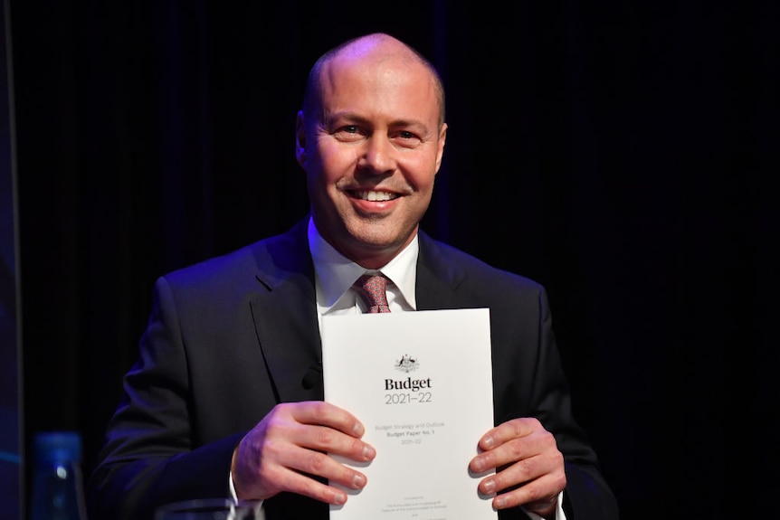 A very smiley Josh Frydenberg holds the budget in front of him.
