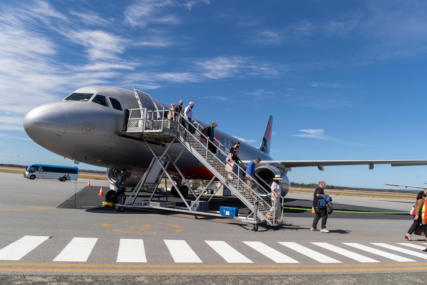 A grey plane on a runway with passengers disembarking down stairs .