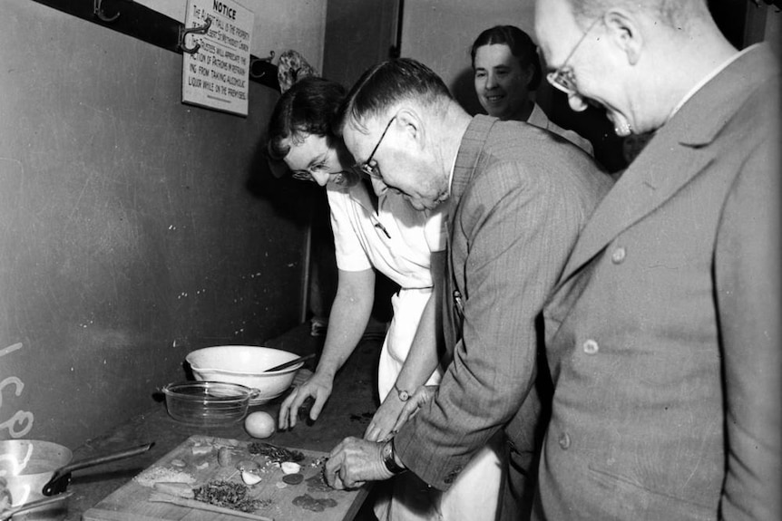 Black and white photo of a man being shown how to cook.
