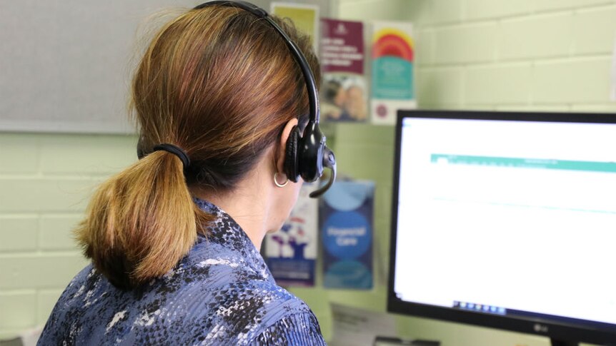 A person wearing a headset looking at a computer screen taken from behind.