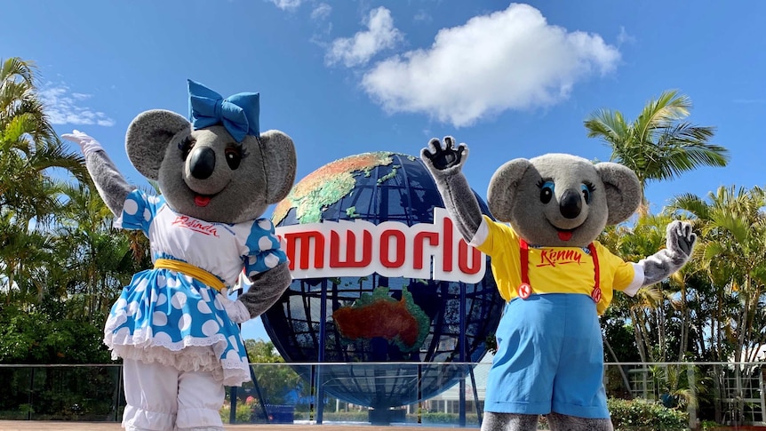 Two people in giant koala costumes stand waving their arms in front of a globe that reads "Dreamworld".