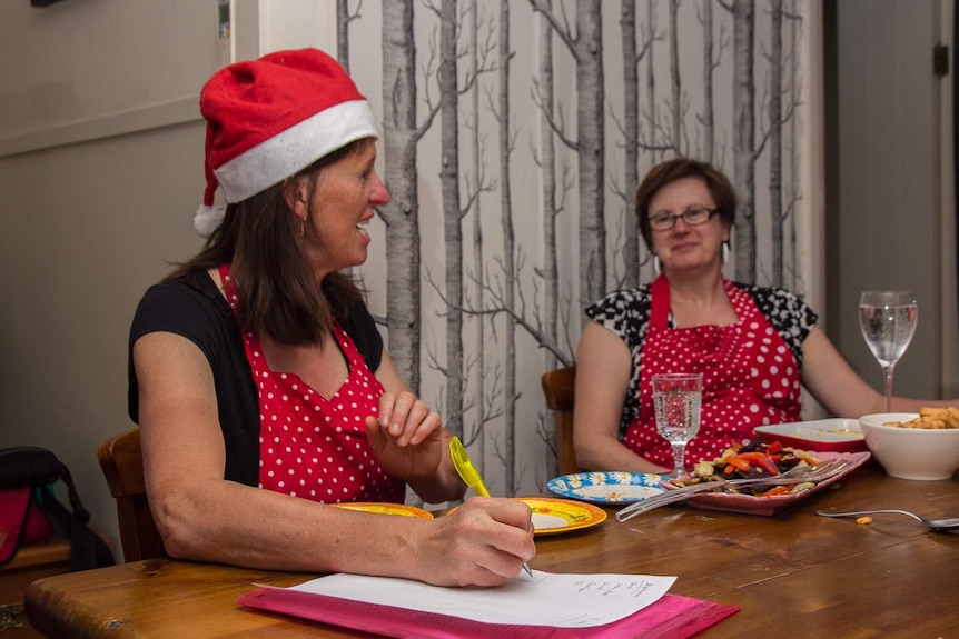A woman in a santa hat and dotted apron holding a pen writing