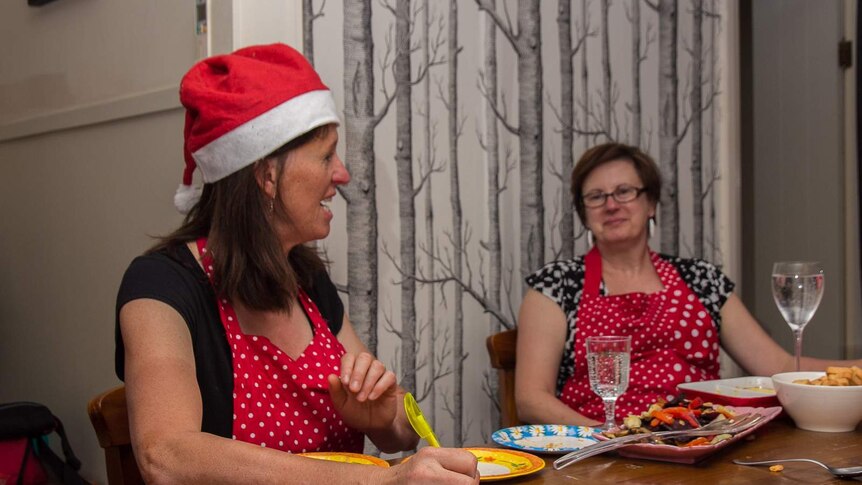 A woman in a santa hat and dotted apron holding a pen writing
