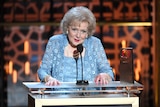 A woman in a blue top and shall accepting an award on a podium 