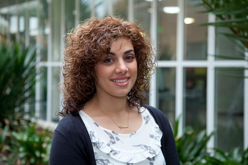 A woman with curly brown hair smiles to camera