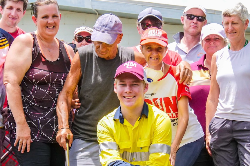 A teenage boy kneels before a group of adults, all hot after cleaning out a flooded house.