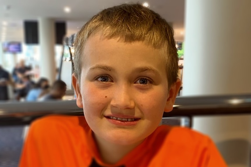 A boy with a bright orange shirt smiles at the camera
