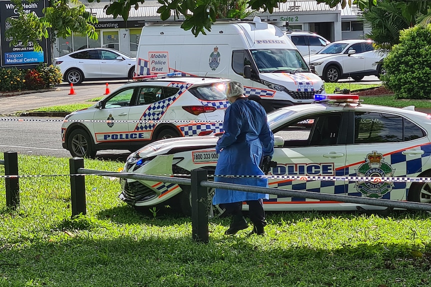 A person in scientific clothes looks at a crashed police car.