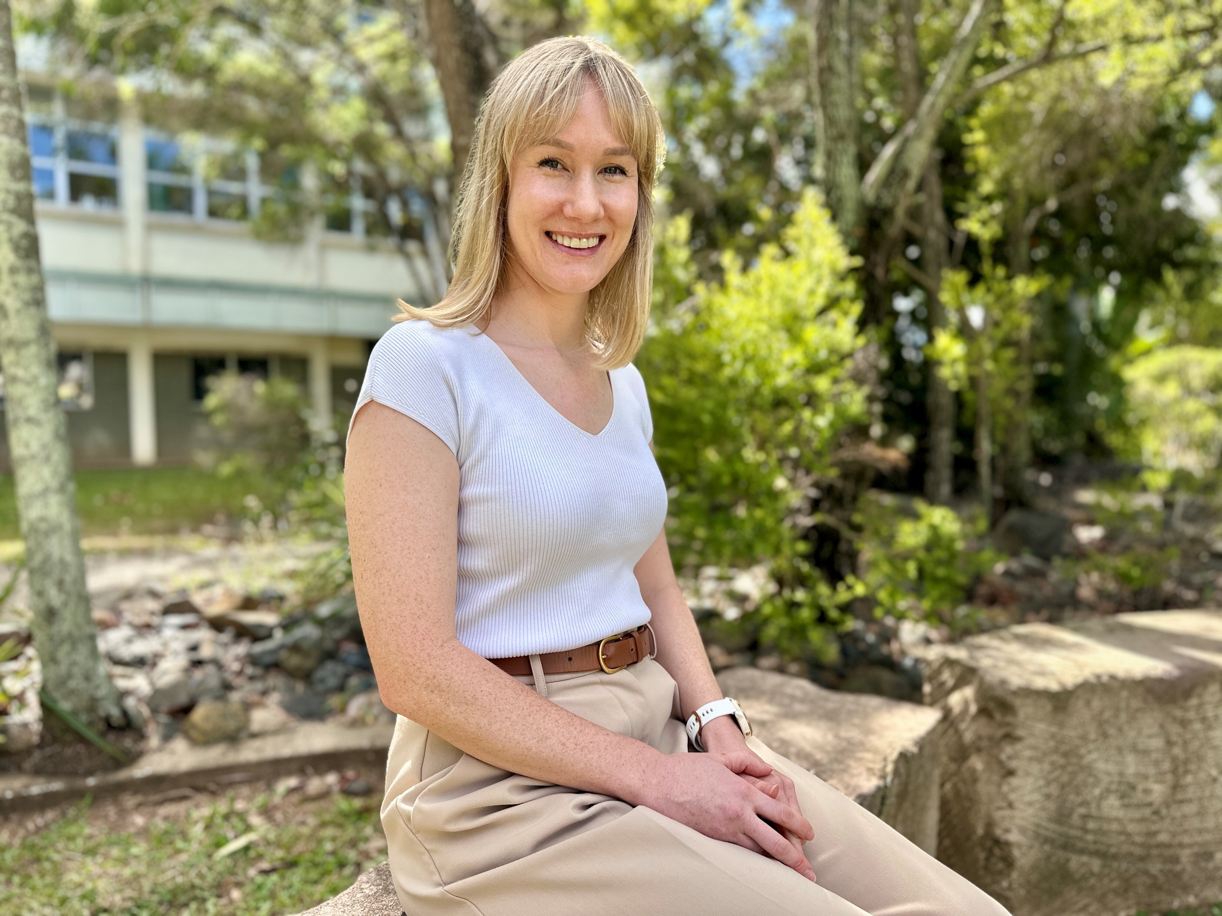 A university lecturer with a white shirt sitting in a garden setting outside a building.
