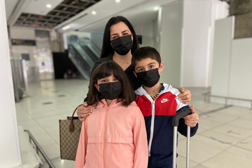 Woman girl and boy in black masks look to camera.