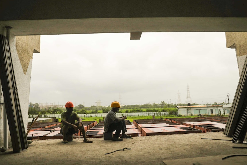 Two men in hard hats since in the window of a half-built building