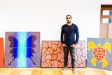 A young man stands in front of vibrant artwork.