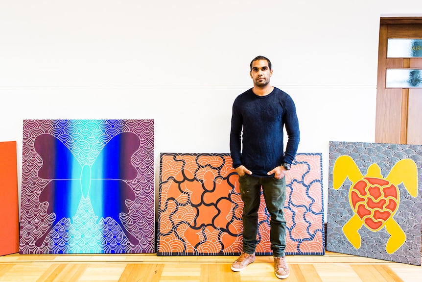 A young man stands in front of vibrant artwork.