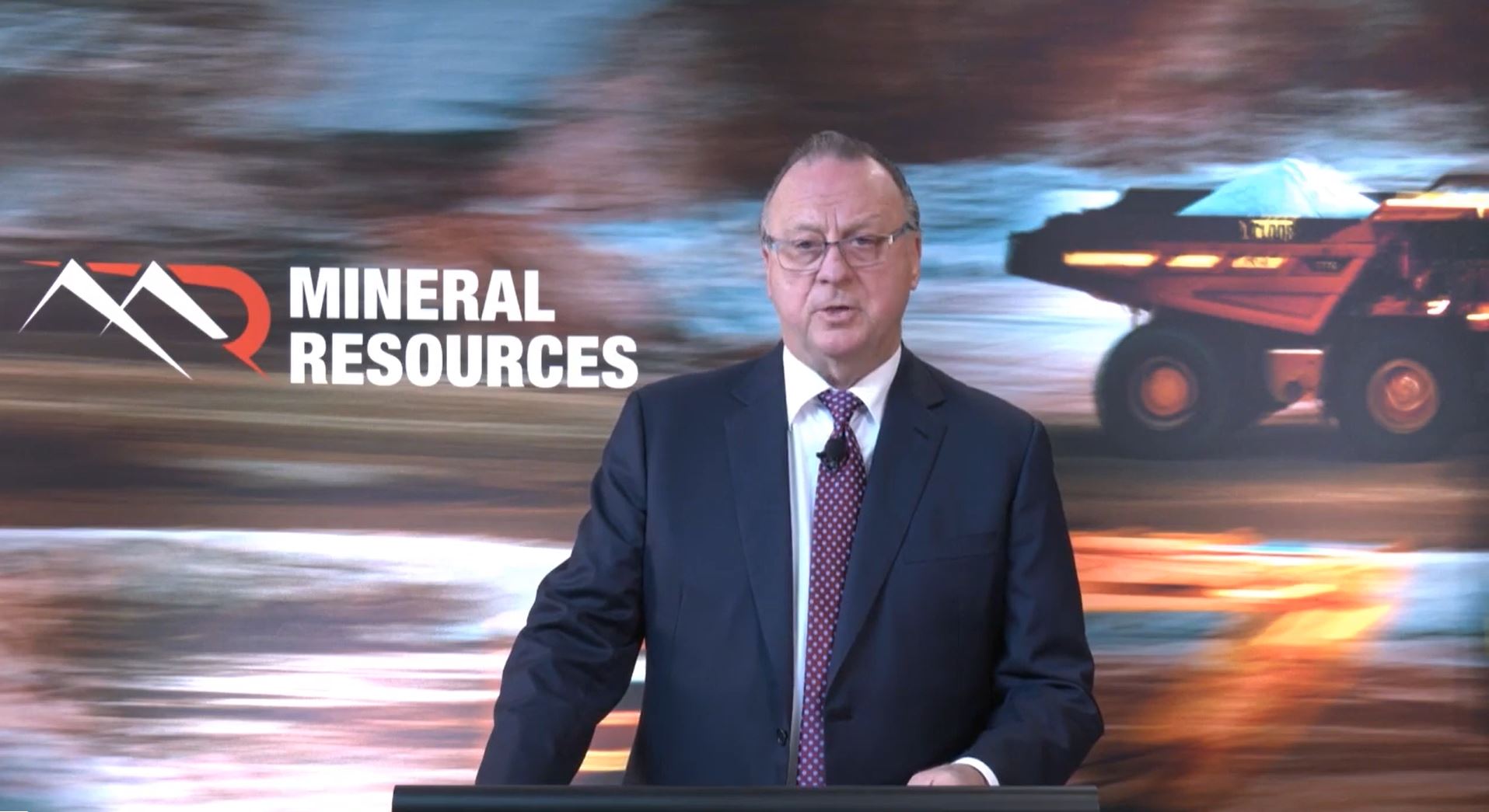 A screen shot of a video conference with a man in a suit and tie is speaking.  