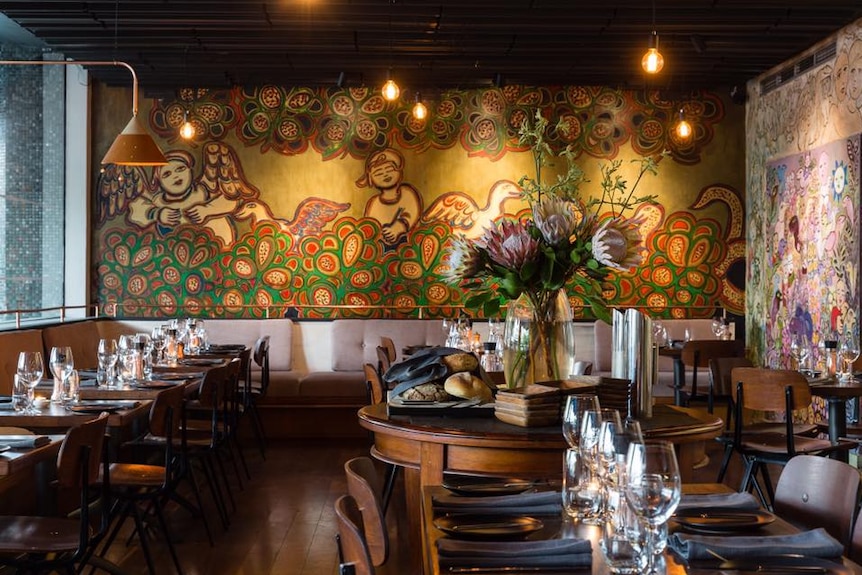 Restaurant interior displaying chairs and table and the mural of artist Mirka Mora