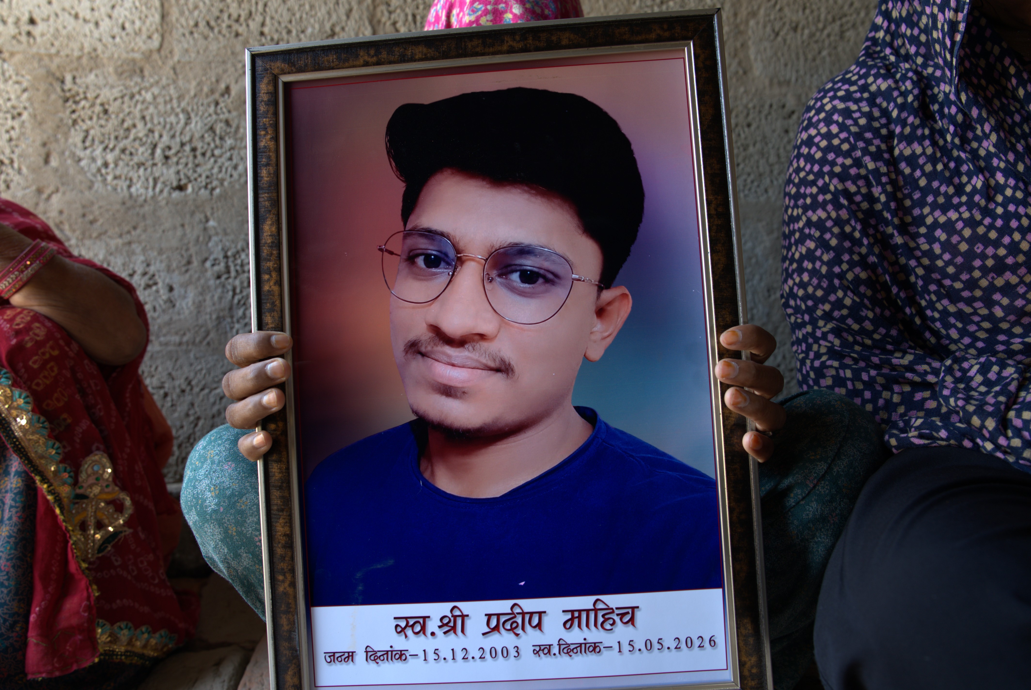Three women hold a framed photo of a young man wearing glasses in a portrait.