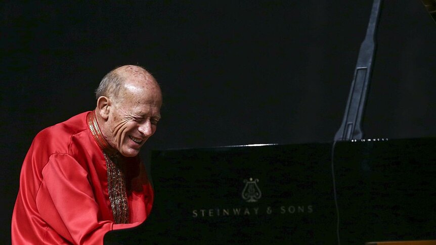 Pianist David Helfgott plays a grand piano wearing a bright red tunic.