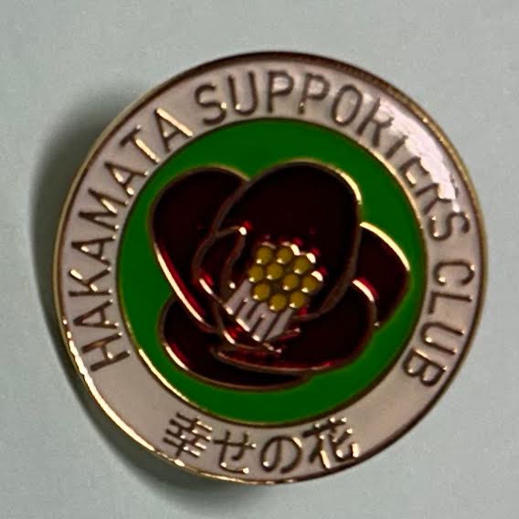 A circular, steel badge with a red flower in the middle.