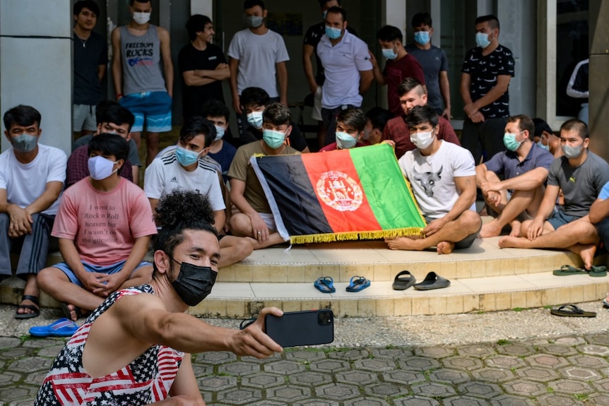 An Afghan refugee takes a selfie while his friends unfurl their country's flag