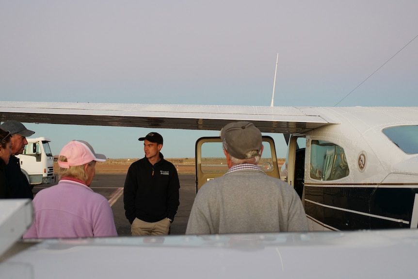 Jonathan Rae beside a cesna 210 plane doing a safety debrief with tourists. 