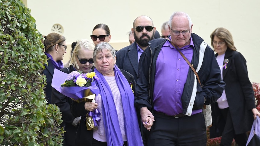 A woman dressed in purple holding flowers supported by friends and family in purple 