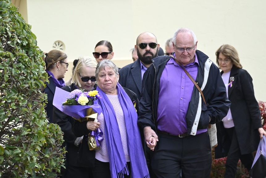 A woman dressed in purple holding flowers supported by friends and family in purple 