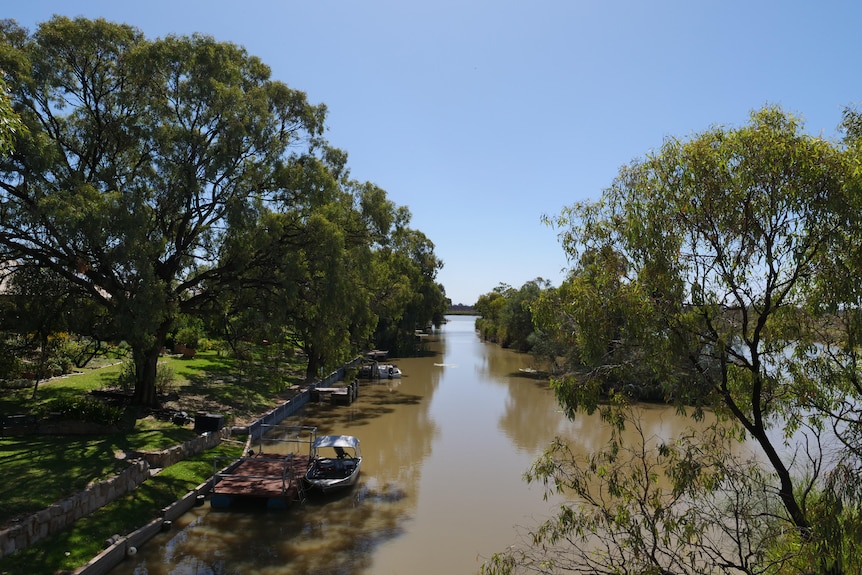 A creek flows past small boats and trees.