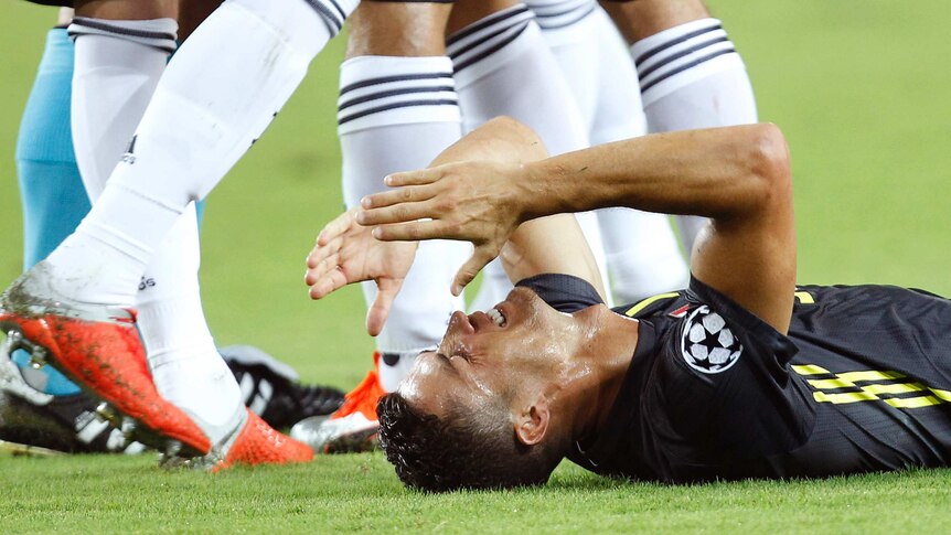 A footballer brings his hands to his face lying down on his back on the grass