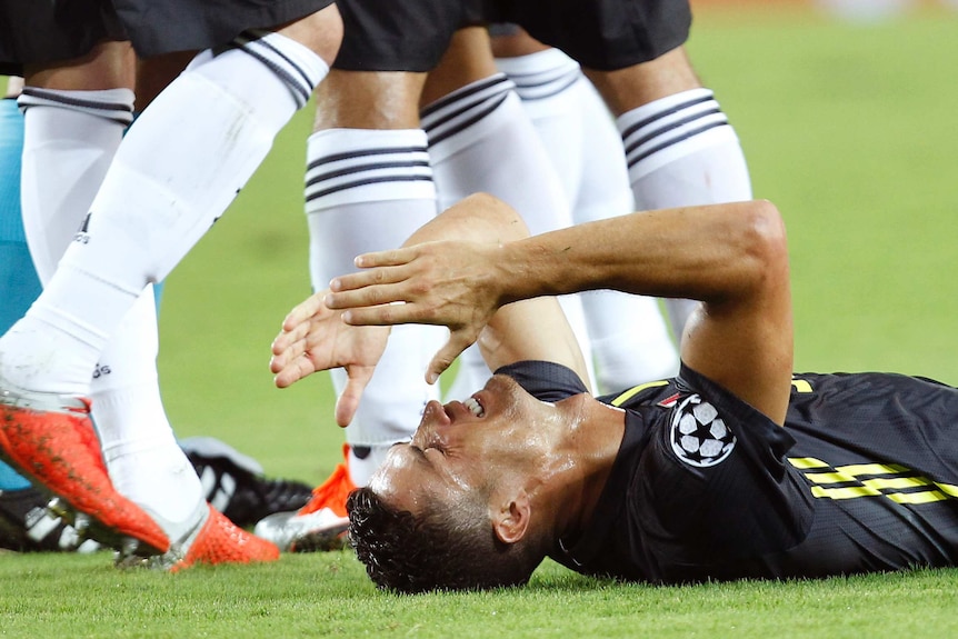 A footballer brings his hands to his face lying down on his back on the grass