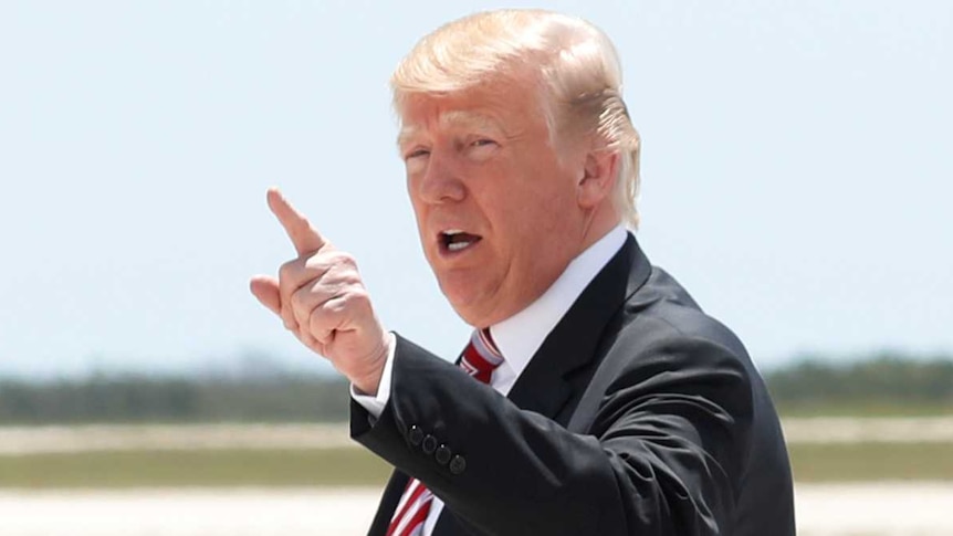 Donald Trump points while wearing a suit on after disembarking from a plane.