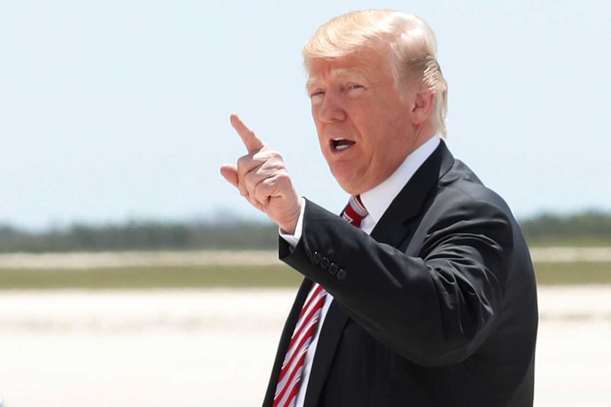 Donald Trump points while wearing a suit on after disembarking from a plane