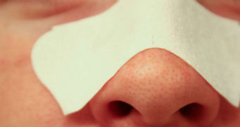 Pores visible on the nose of a woman using a blackhead strip.