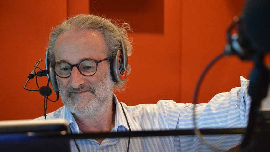 Jon Faine wearing headphones and looking at computer screen in radio studio.