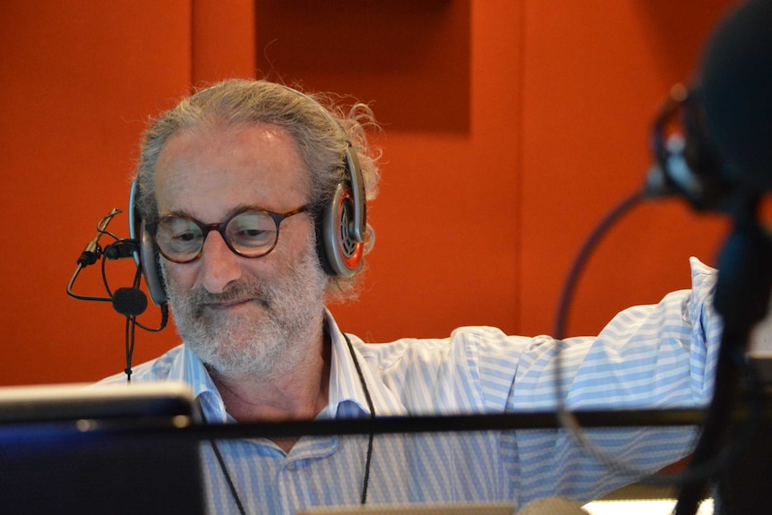 Jon Faine wearing headphones and looking at computer screen in radio studio.