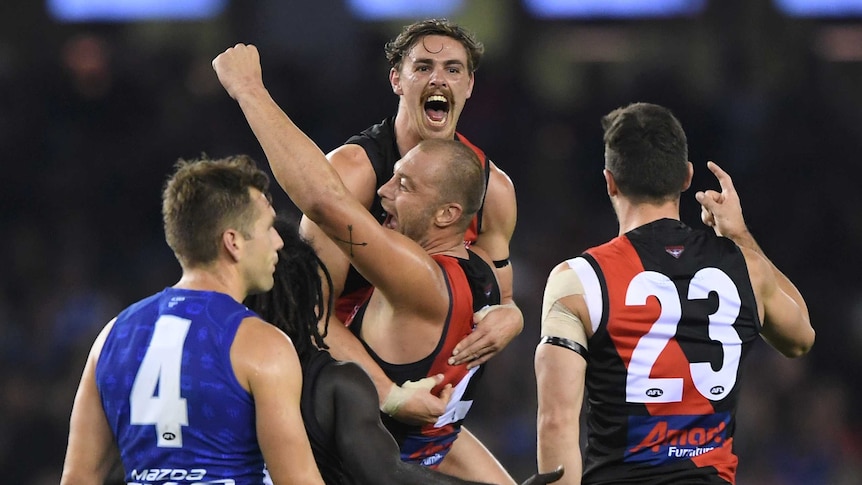 An AFL player lifts his goalscoring teammate in the air in celebration.