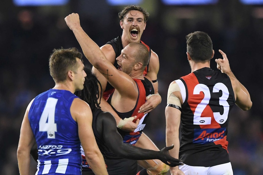 An AFL player lifts his goalscoring teammate in the air in celebration.