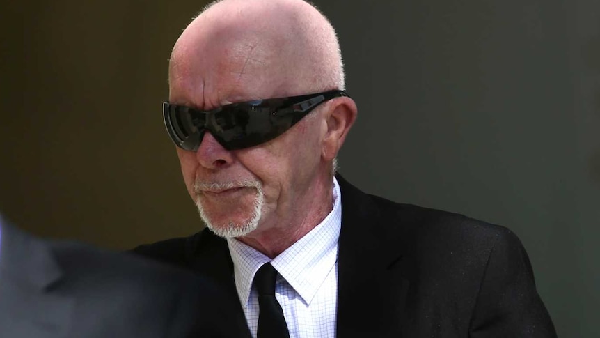 A man in a suit and sunglasses walks into court.