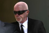 A man in a suit and sunglasses walks into court.