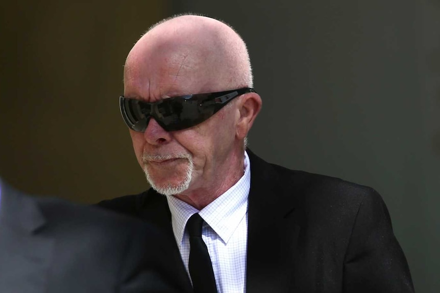 A man in a suit and sunglasses walks into court.