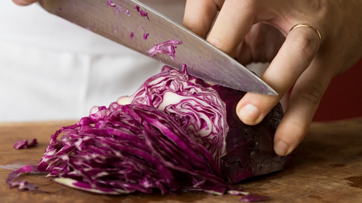 A man cutting into a red cabbage with a large kitchen knife.