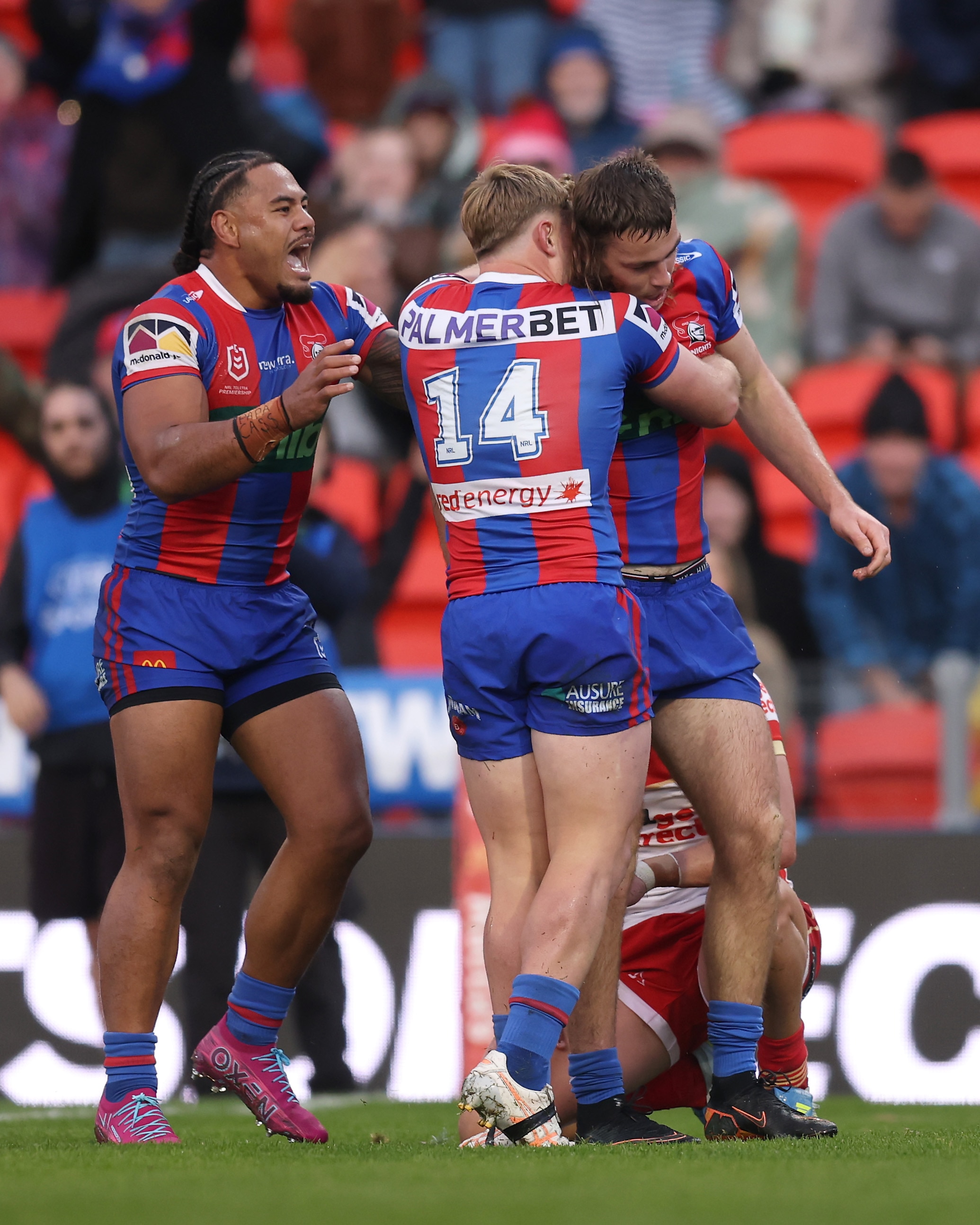 A group of rugby league players in red and blue stripes celebrate a win, hugging each other