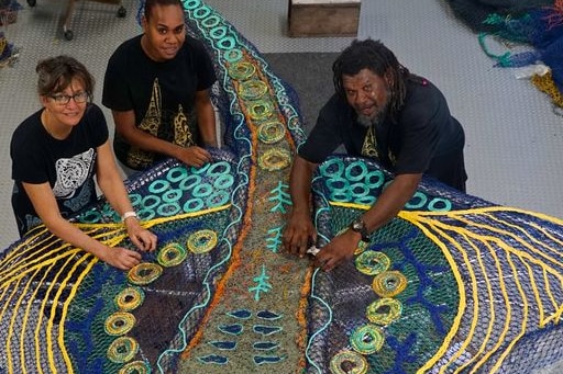 3 artists standing next to a n eagle ray art piece crafted from ghost nets