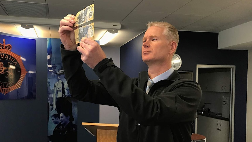 Tasmania Police Detective Inspector Jon King compares real and counterfeit $50 notes