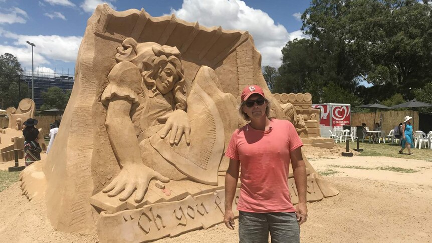 A man stands in front of a sand sculpture.
