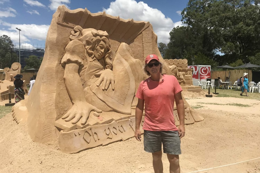 A man stands in front of a sand sculpture.