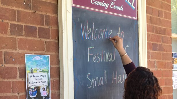 A woman writes 'welcome to Festival of Small Halls' on a blackboard.