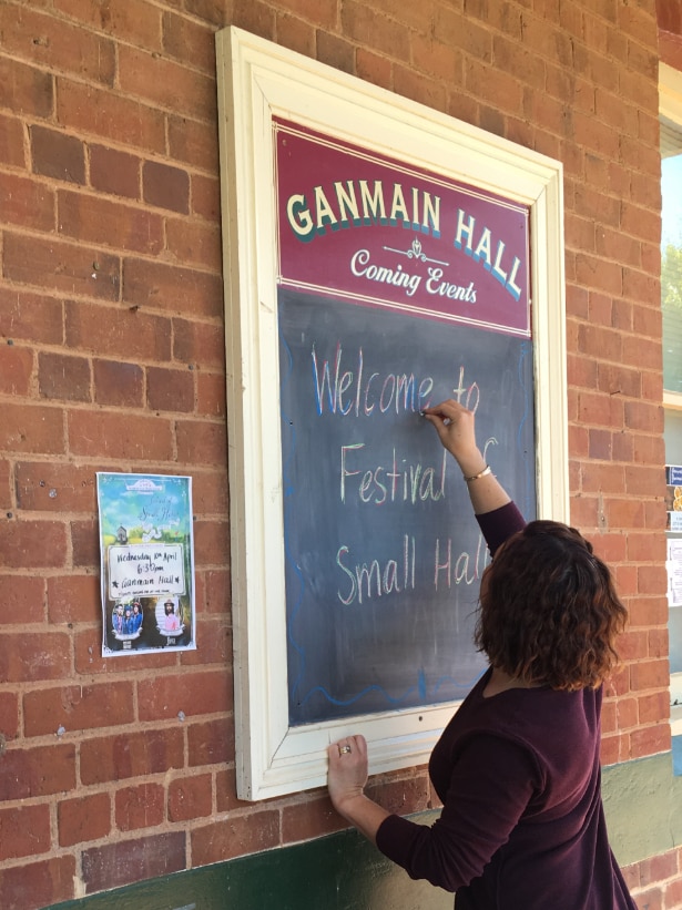 A woman writes 'welcome to Festival of Small Halls' on a blackboard.