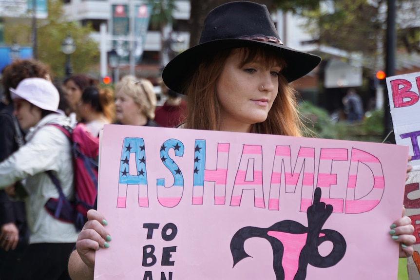 US citizen Sarah Fhay holds a sign saying she's ashamed to be American.