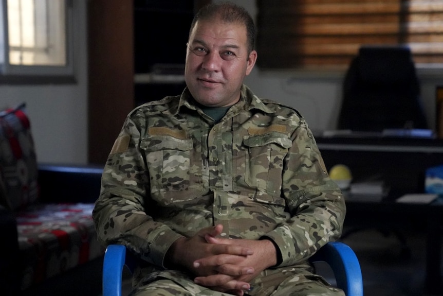 A middle-aged man in army camouflage, smiling at the camera.