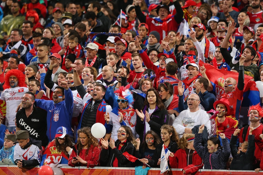 A crowd wearing Serbian colours cheers during a sports match